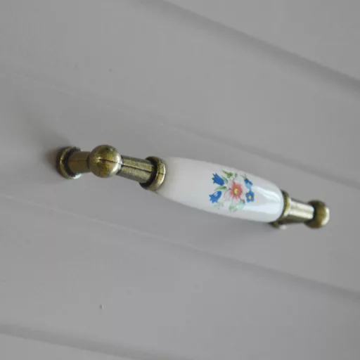 Porcelán-fém bútorfogantyú, antik bronz-színes virággal, 96 mm furattávval